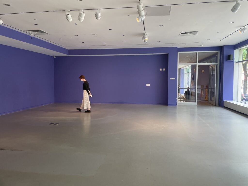Empty gallery space with a single person standing near the center of the room.